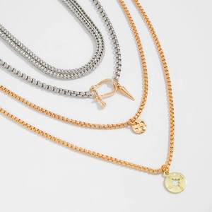 Detail of layered gold and silver chains with compass star pendant and U-shaped buckle
