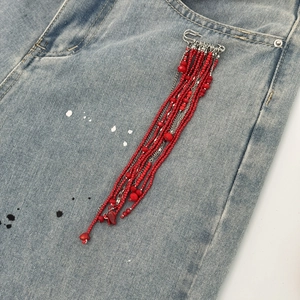 Detail of red beaded fringe brooch pin pinned on denim pocket with silver chain
