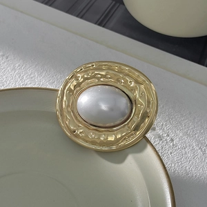 Dettaglio di una spilla vintage in metallo dorato con un grande intarsio di perla ovale