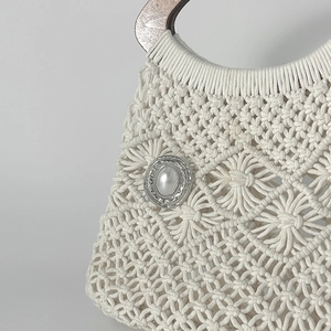 Dettaglio borsa intrecciata con spilla cigno in metallo liquido e decorazione di perle