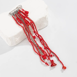 Détail d'une broche pompon à perles rouges avec chaînes argentées et pierres sur pierre