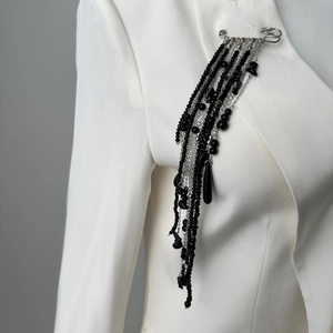 Close-up of hip hop beaded tassel brooch with silver chains and black crystals on white suit
