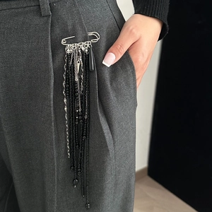Détail d'une broche épingle avec pompons perlés noirs sur un pantalon de costume gris
