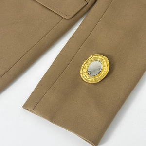 Dettaglio di un bottone metallico irregolare sulla manica di un blazer kaki in twill