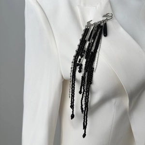 Detailed view of a long tassel brooch with black beads on a white blazer lapel