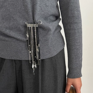Broche épingle argentée avec longues chaînes à pompons et perles sur un pull en maille