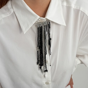 Détail d'une broche aile d'ange vintage avec pompons en cristal noir sur une chemise