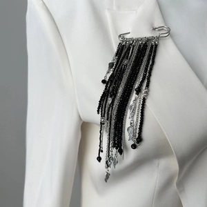 Detail of silver safety pin brooch with black beads, tassel chains, and wing charm