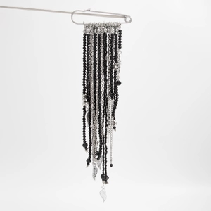 Detail of gothic style safety pin brooch with black beads, silver chains and feather charms