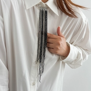 Gros plan d'une broche à franges en perles noires et argentées sur un col blanc