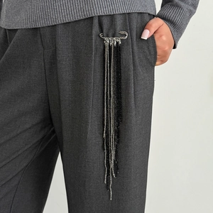 Detailed view of silver safety pin brooch with long black and grey beaded tassels on pants
