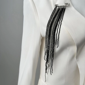 Detailed view of long black beaded tassel brooch pinned on a white blazer lapel