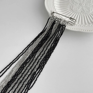 Détail d'une broche épingle avec de longues franges en perles de cristal noir et gris