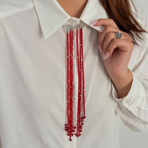 Détail de la broche à glands en perles rouges et chaînes sur col de chemise blanche