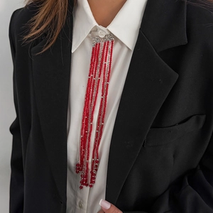 Long tassel brooch with vibrant red beads and silver metal chains on a black suit jacket