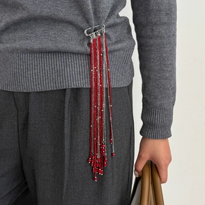 Détail de la broche à pompons de perles rouges et chaînes argentées sur un pull gris