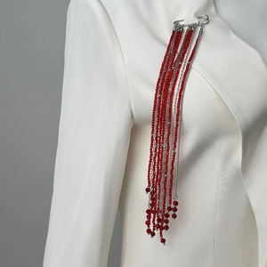 Détail de broche à pampilles en cristal rouge avec épingle sur un revers de veste blanc