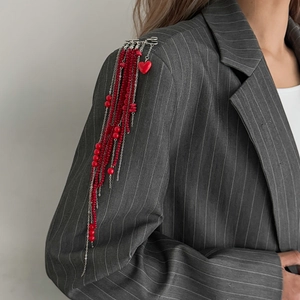 Vue détaillée d'une broche d'épaule avec perles rouges et pendentif cœur sur un costume gris
