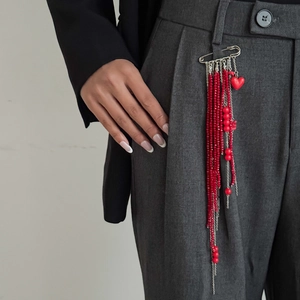 Detail of a hip-hop style safety pin brooch with red beaded fringe on a grey suit