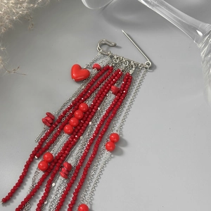 Détail d'une broche à pompon en perles rouges avec breloque cœur et chaînes argent