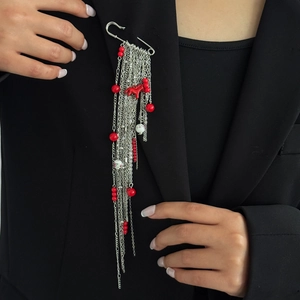 Détail d'une broche à pompons argentés avec perles rouges sur un revers noir