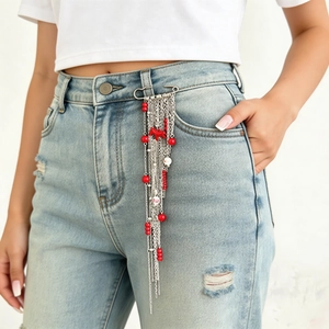 Détail d'une broche épingle avec perles rouges et chaînes à franges sur un jean bleu