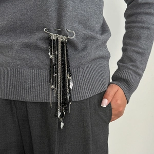 Detail of beaded tassel brooch with silver wings and black beads on grey sweater