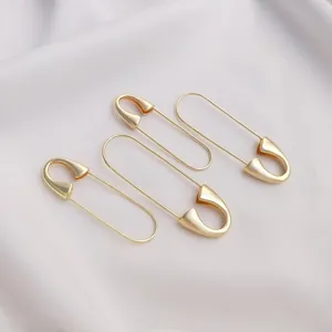 Close-up of three polished 14K gold-plated safety pins on white fabric background