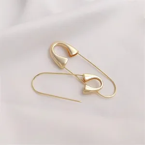 Elegant pair of 14K gold-plated safety pin earrings on a soft white pleated background