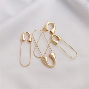 Polished 14K gold plated safety pin accessories on elegant white silk fabric