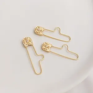 Detail of 14K gold plated safety pin pendant with embossed cross floral and zircon