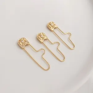 Close-up of 14K gold plated safety pin pendants with embossed flowers and tiny zircons