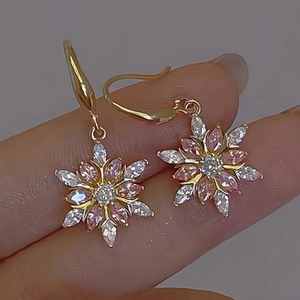 Mano che regge eleganti orecchini a fiocco di neve in oro con zirconi rosa e bianchi