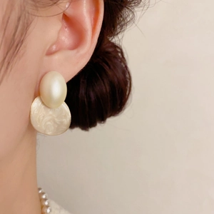 Détail de boucles d'oreilles ovales vintage avec perles crème et effet marbre