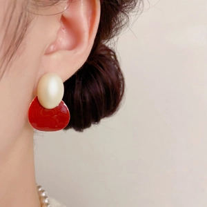 Gros plan de boucles d'oreilles ovales avec perles beiges et émail rouge sur le modèle