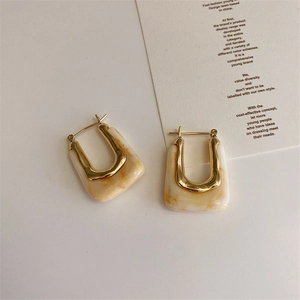 Close-up of geometric U-shape gold metal earrings with marble texture resin inlay