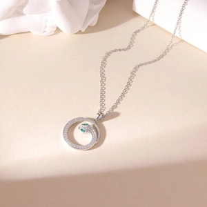 Zilveren slangenketting met groene ogen en witte stenen op een minimalistische basis