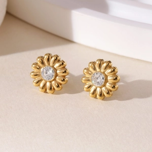 Golden daisy stud earrings with sparkling zircon centers on a minimalist beige background