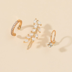 Detailed close-up of three-piece gold leaf and zircon ear cuff set on beige background