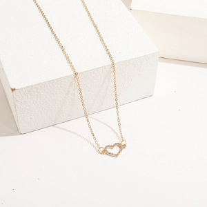Elegante collar con colgante de corazón dorado y cristales sobre un pedestal blanco