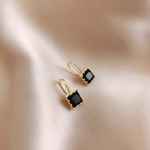 Elegante goldene quadratische Ohrringe mit schwarzen Edelsteinen auf Champagnerseide