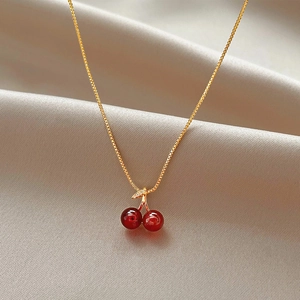 Dettaglio del ciondolo a ciliegia con perline rosse e foglia brillante su raso oro