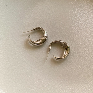 Irregular silver C-shaped lava hoop earrings with a minimalist molten metal texture finish