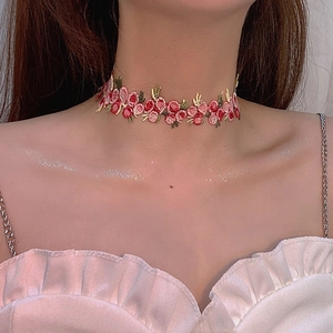 Gros plan d'un choker brodé de fleurs roses et rouges avec des feuilles vertes délicates