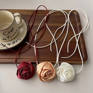 Tre choker a rosa in seta in rosso, champagne e bianco esposti su un vassoio di legno