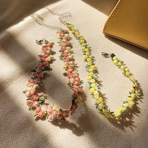 Gros plan sur la broderie florale et le fermoir mousqueton argenté du collier ras du cou