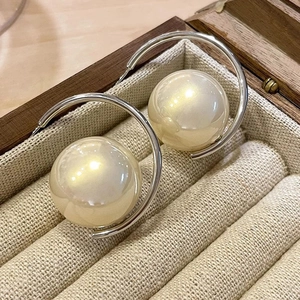 Macro detail of large faux pearl earrings with polished silver metal arc on linen background