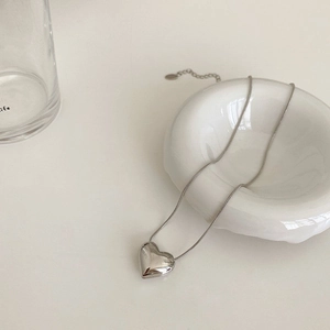 Macro shot of silver puffy heart pendant with snake chain on white ceramic tray