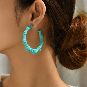 Detail of matte teal bamboo-shaped C-hoop earring worn by a model for fashion context
