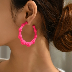 Close-up of neon pink bamboo texture hoop earrings worn by a fashion model